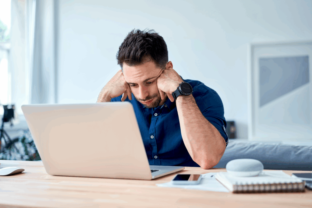 A man sits at a table, looking frustrated while staring at his laptop, conveying the emotional toll of updates.